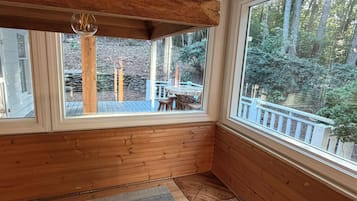 Une pièce aux murs en bois et aux grandes fenêtres donnant sur une terrasse et une forêt.