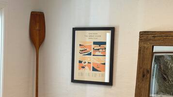 Ein gerahmtes Poster an einer Wand, ein hölzernes Paddel, das an die Wand gelehnt ist, und ein gerahmtes Bild zur Rechten.