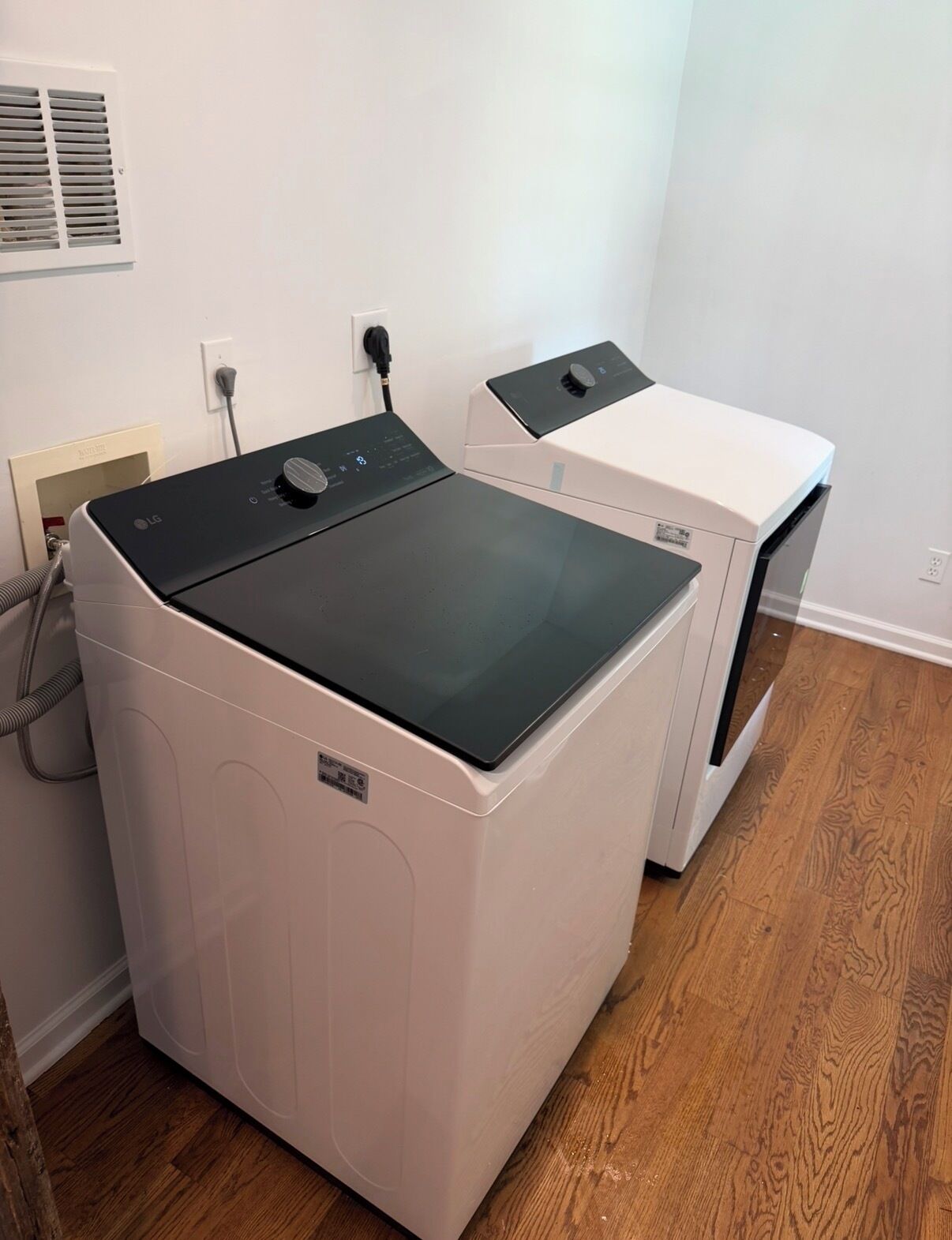 A laundry room with two stacked washers and dryers, a power outlet, and a vent on the wall.