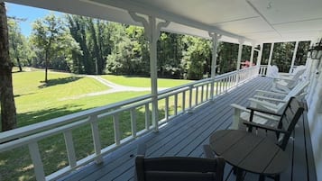 A covered outdoor area with a wooden deck, white railings, and a view of a grassy lawn.