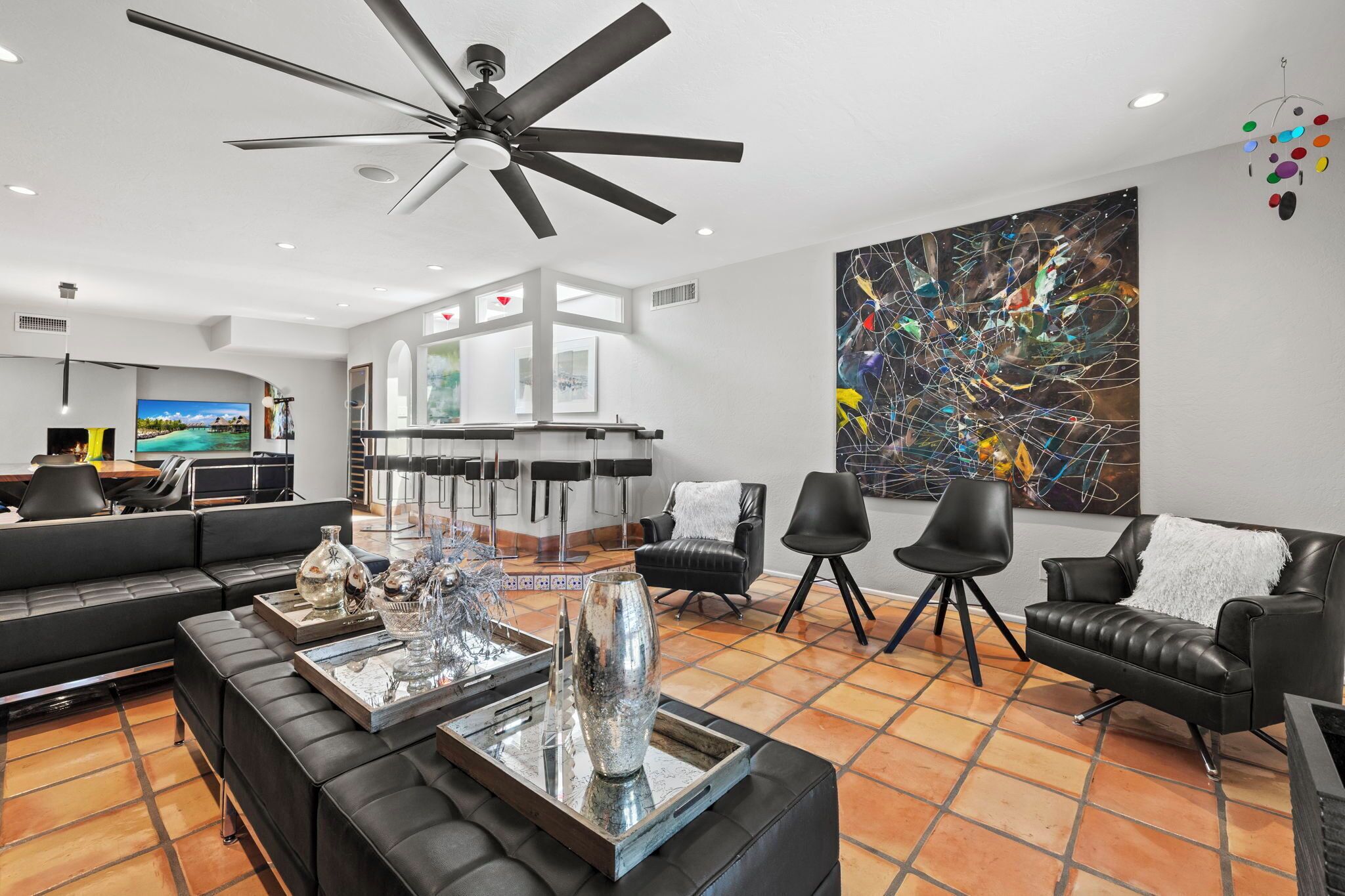 Un soggiorno moderno con ventilatore a soffitto, divani in pelle nera, un tavolino da caffè con oggetti decorativi e un grande quadro astratto appeso al muro.