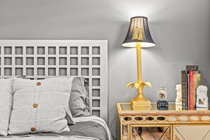 Uma cama bem arrumada com cabeceira, abajur e uma pequena mesa de cabeceira de madeira com livros e objetos decorativos.
