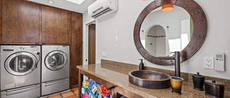 A modern bathroom with a large mirror, a sink, and two wall-mounted washing machines.