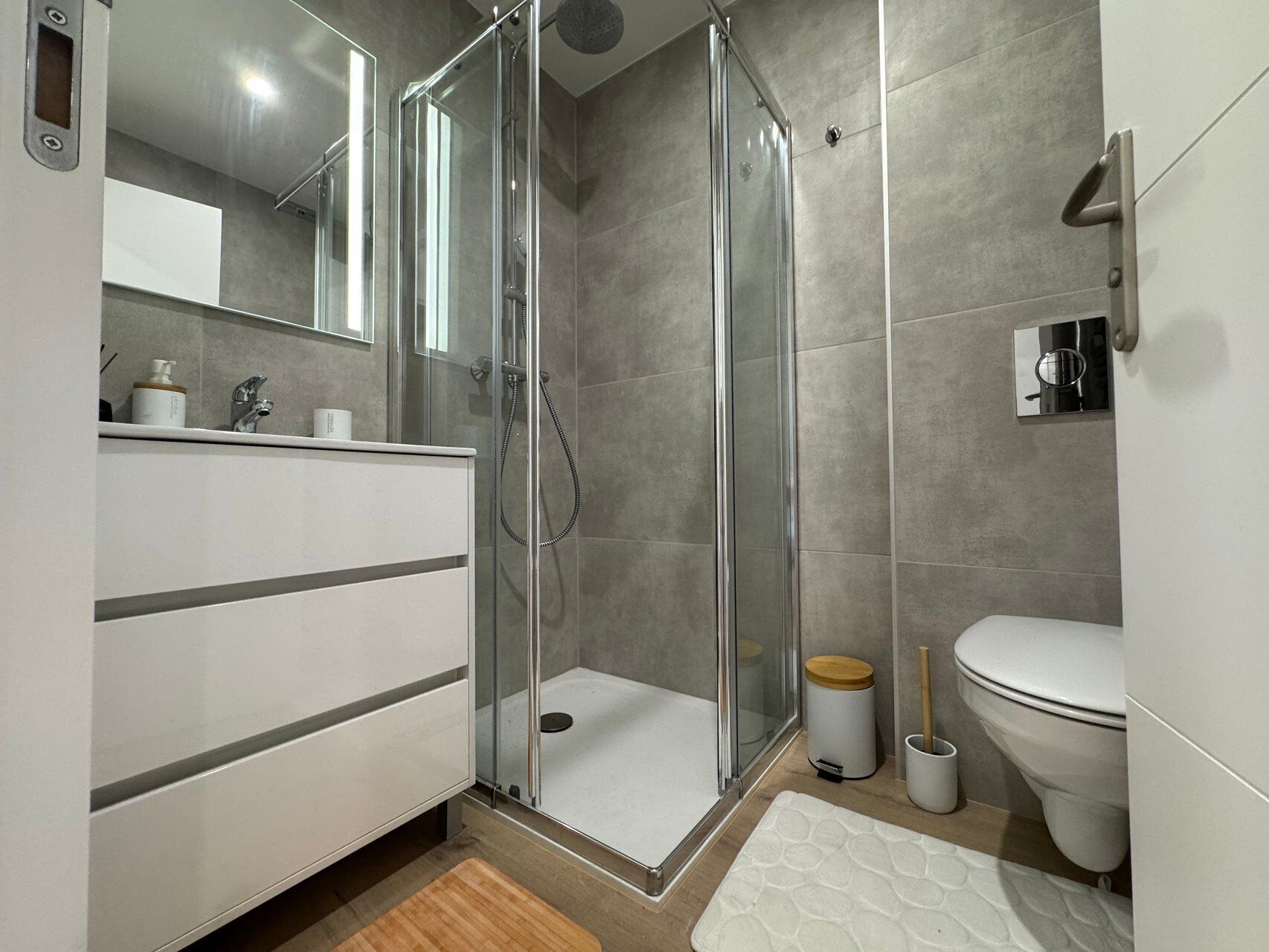 Une salle de bain moderne avec une douche à parois de verre, des toilettes et un lavabo surmonté d’un miroir.