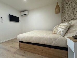 A bedroom with a bed, a mounted air conditioner, a flat-screen TV, and a decorative wall panel. - Le Petit Coin Bohéme, 4 pers, pieds dans l'eau (Le Cap d'Agde)