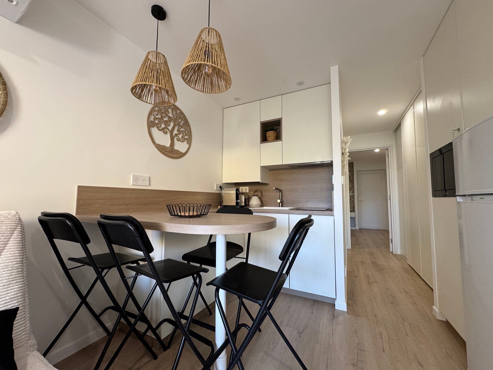 A modern kitchen with a round dining table, black chairs, and a hanging light fixture.