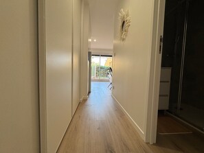 A hallway with a wooden floor, a door on the right, and a view of a balcony with a garden. - Le Petit Coin Bohéme, 4 pers, pieds dans l'eau (Le Cap d'Agde)