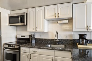 A kitchen with white cabinets, a stainless steel microwave, a gas stove, a sink, and a coffee maker. - City view oceanfront Ilikai condo. (Honolulu)