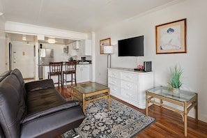 Un salon comprenant un canapé, une table basse en verre, un tapis à motifs, un meuble blanc, un téléviseur à écran plat et un tableau encadré accroché au mur.
