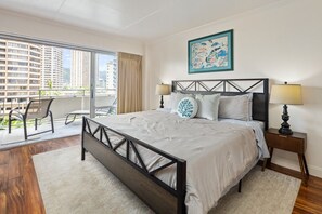 Ein Hotelzimmer mit einem großen Bett, einem Nachttisch, einem Sessel und einem Fenster mit Blick auf Gebäude.