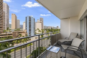 Un balcon avec une table et des chaises, donnant sur un paysage urbain avec de hauts immeubles et des palmiers.