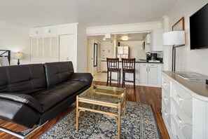 A living room with a black leather sofa, a glass coffee table, a patterned rug, a white cabinet, and a flat-screen TV. - City view oceanfront Ilikai condo. (Honolulu)
