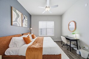 A bedroom with a bed, a desk, a chair, a ceiling fan, and a window. - Modern 2BR Apartment with Pool, Gym & Free Parking (Houston)