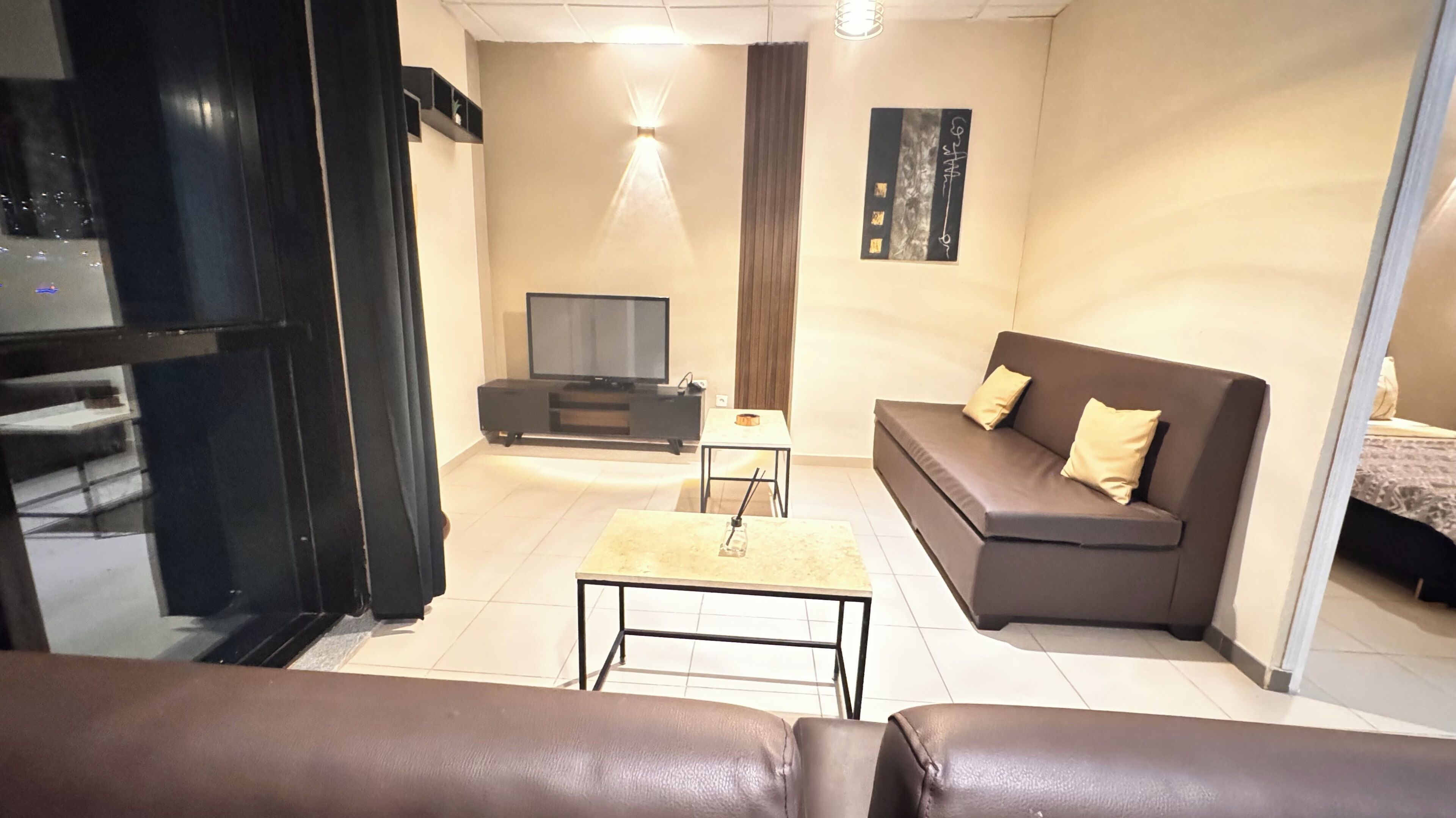 Uma sala de estar moderna com um sofá, uma mesa de centro, uma televisão e uma pequena mesa com abajur.