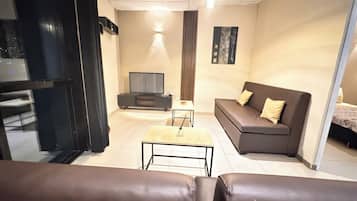 Uma sala de estar moderna com um sofá, uma mesa de centro, uma televisão e uma pequena mesa com abajur.
