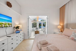 A hotel room with a bed, a TV, a desk, and a view of the outdoor area. - Two-home tropical retreat near Palm Beach Zoo (West Palm Beach)