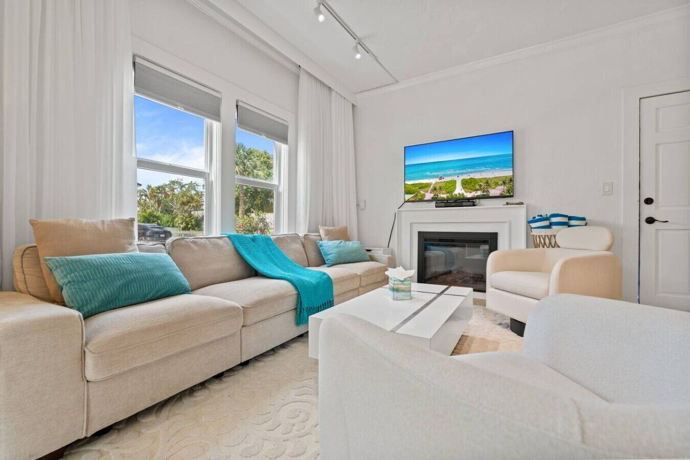 Un salon moderne avec un canapé beige, un fauteuil blanc, une cheminée et une grande fenêtre donnant sur un paysage verdoyant.
