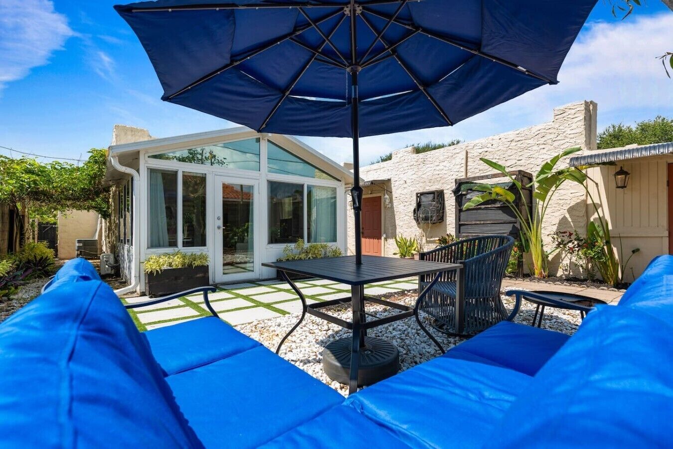 A patio area with a table and chairs, a blue umbrella, and a glass-enclosed structure.