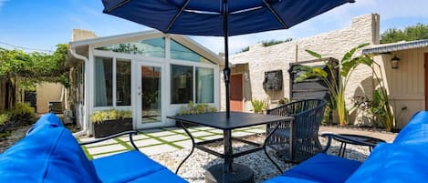 Un espace patio avec une table et des chaises, un parasol bleu et une structure fermée par des parois de verre.