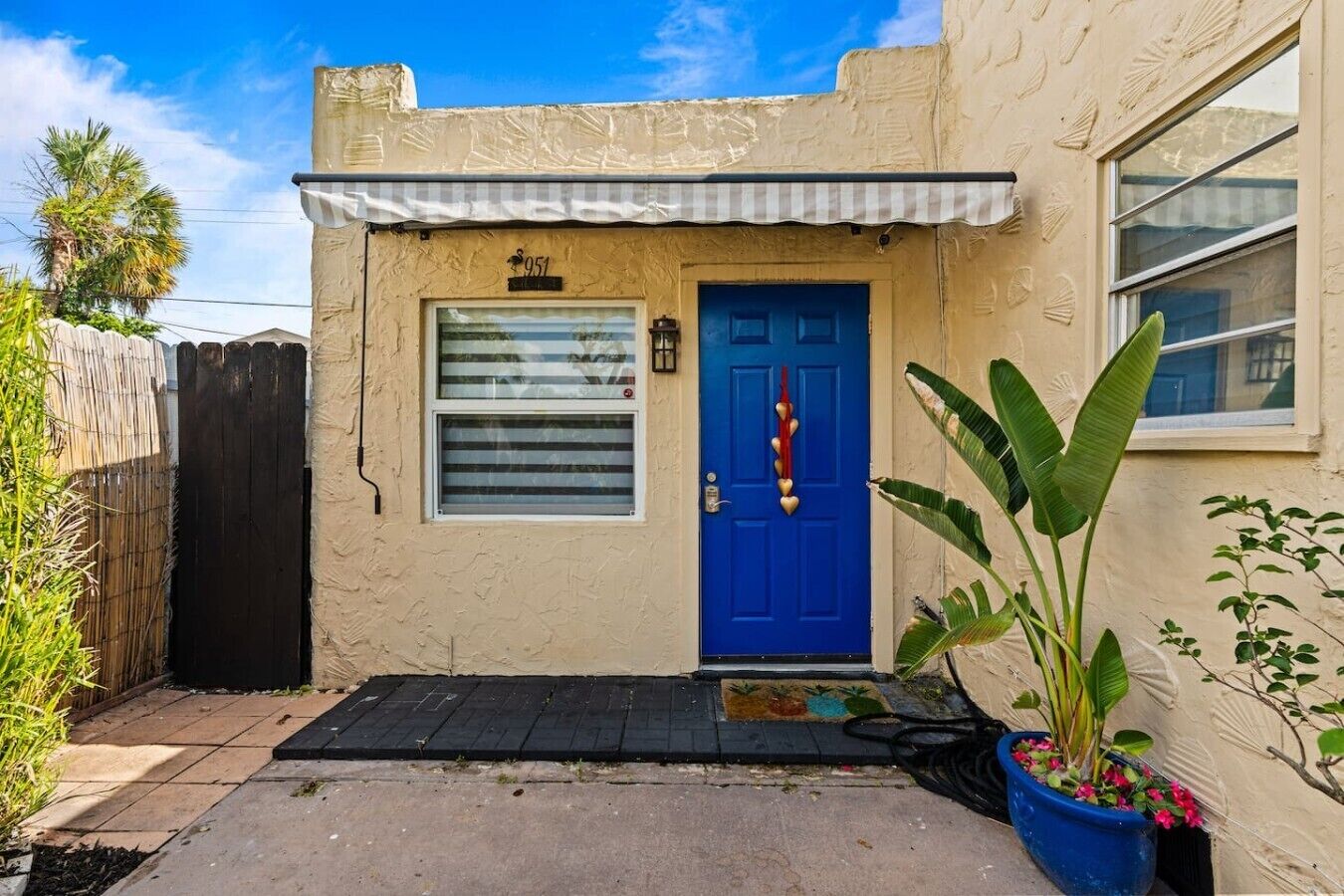A small building with a blue door, a small window with blinds, and a number plaque above the door.