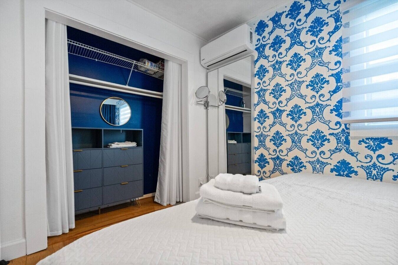 Ein Schlafzimmer mit einem Bett, einem Kleiderschrank, einem Spiegel und einer Wand mit Muster.
