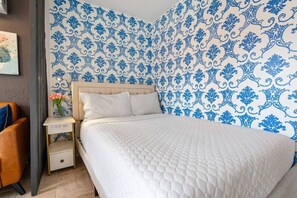 Een slaapkamer met een bed, nachtkastje, stoel en een muur met een blauw patroon.