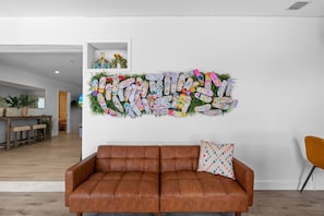 Ein Wohnzimmer mit einer braunen Ledersofa, einem farbenfrohen Wandbild und einer kleinen Vitrine mit Dekoration.