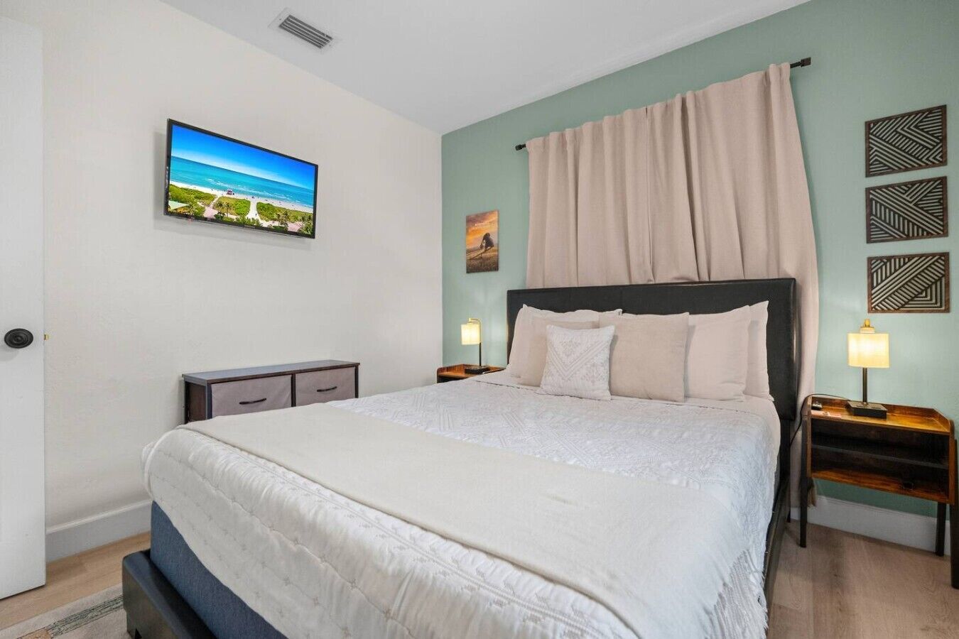 Quarto com cama, mesas de cabeceira, televisão na parede e um quadro.