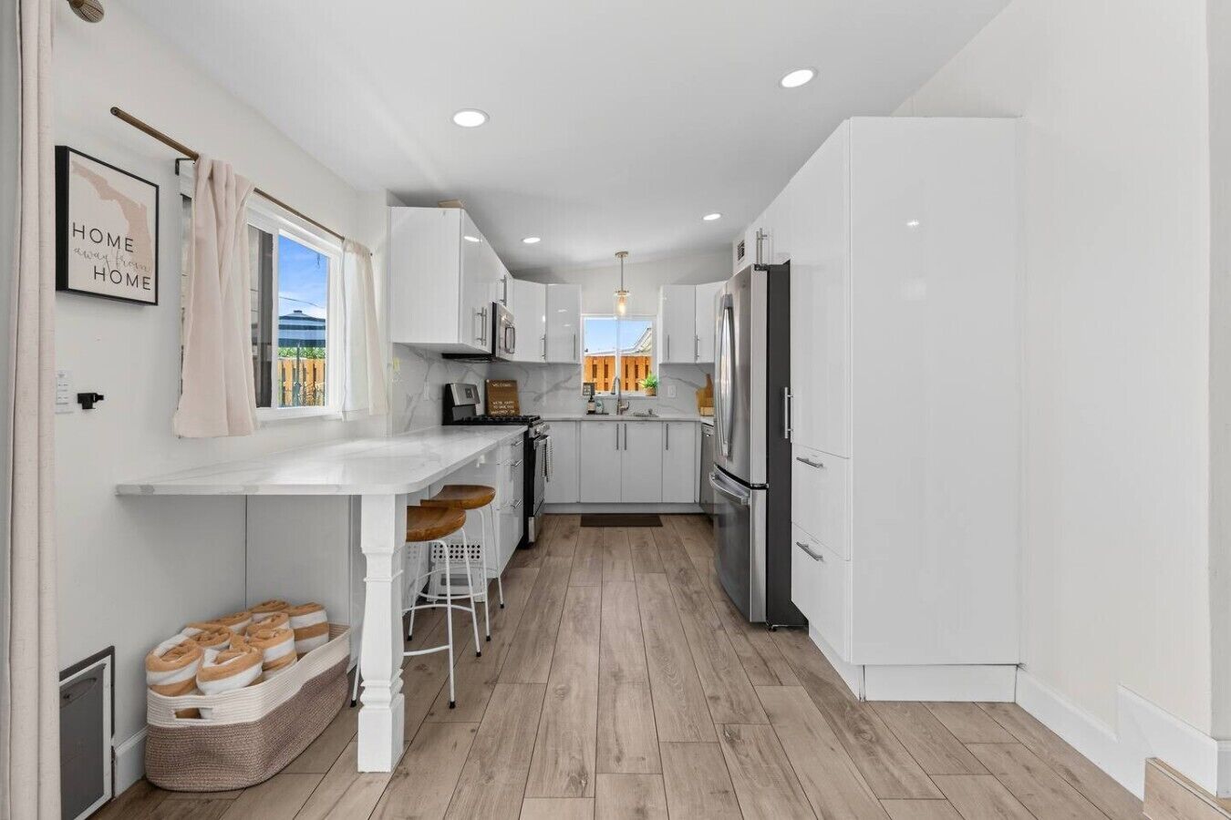 Una cocina moderna con armarios blancos, una isla central con taburetes y vistas al exterior.