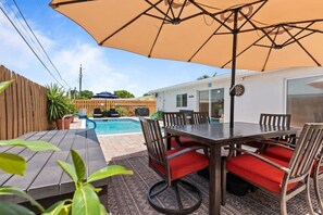 Eine Terrassenanlage im Freien mit Pool, Esstisch und Stühlen sowie einem großen Sonnenschirm.