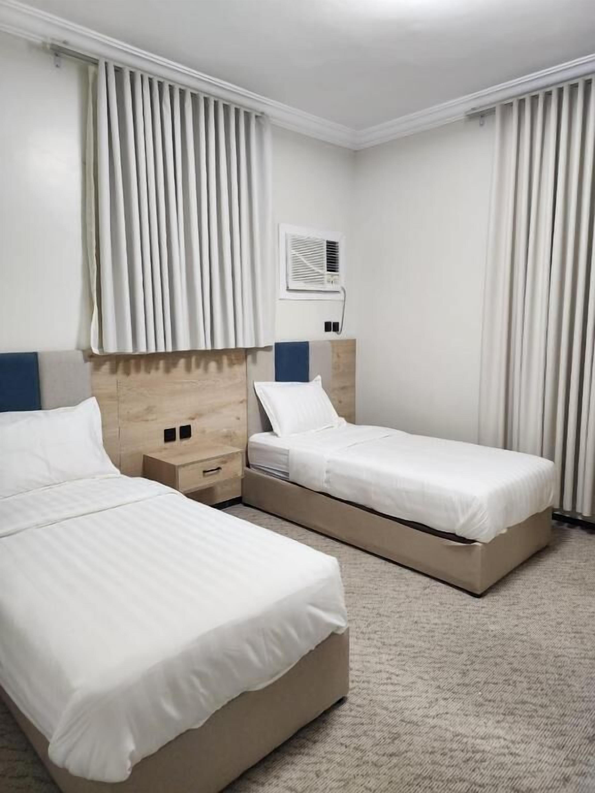 Quarto de hotel com duas camas, cabeceira de madeira, mesa de cabeceira e ar condicionado fixado na parede.