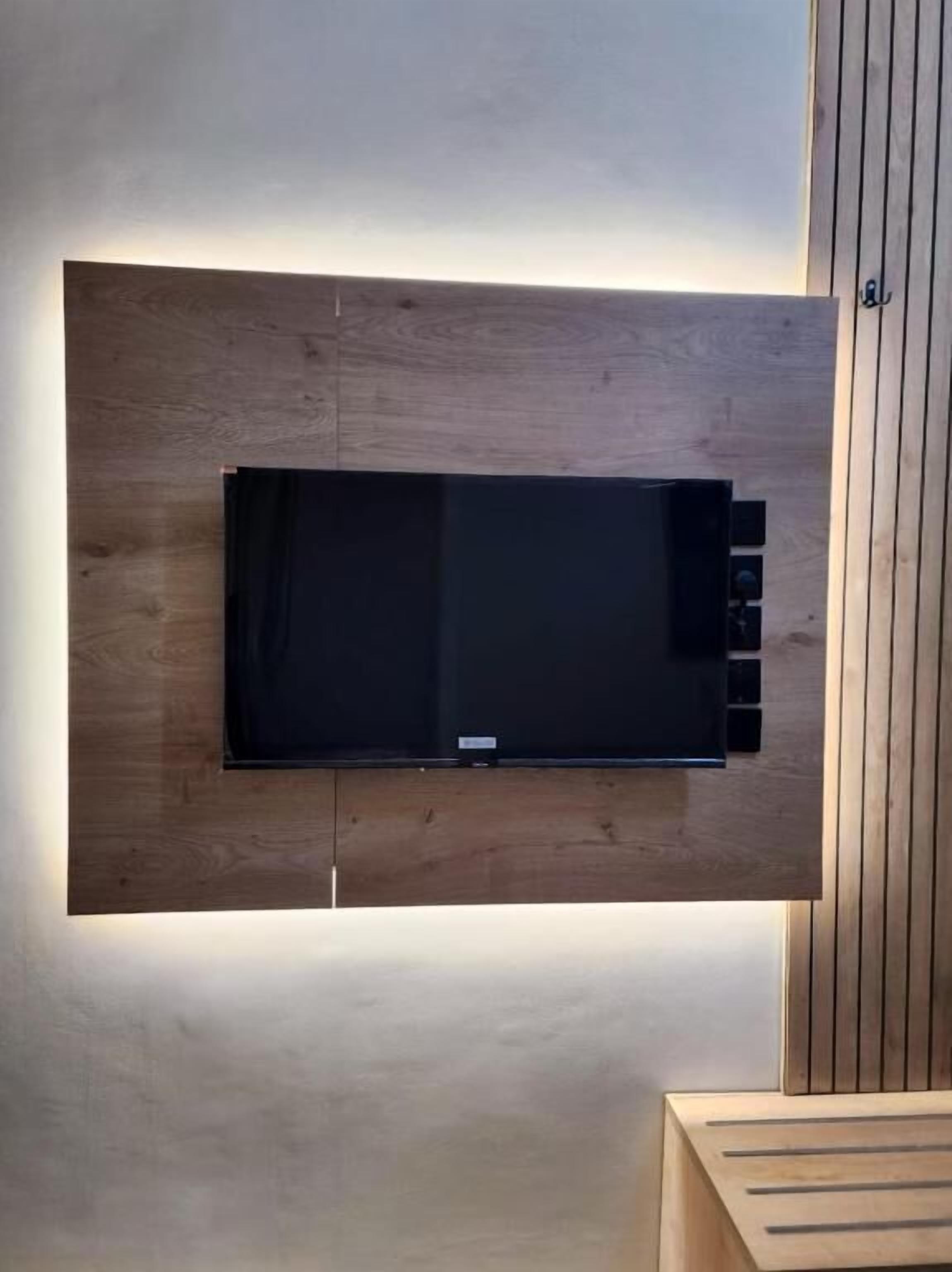 A flat-screen TV mounted on a wooden wall with a wooden panel to the right.