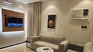 Una sala moderna con una televisión de pantalla plana montada en un panel de madera, un sofá color beige, una mesa redonda de centro y un equipo de aire acondicionado instalado en la pared.