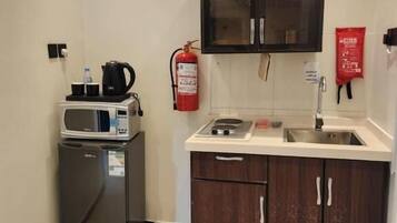 A compact kitchenette with a microwave, coffee maker, and a small refrigerator. There is a fire extinguisher mounted on the wall and a sink with a faucet.