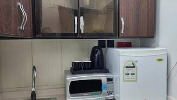 Uma cozinha compacta com micro-ondas, cafeteira e geladeira.