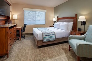 Ein Hotelzimmer mit einem Bett, einem Schreibtisch, einem Sessel, einer Kommode und einem Fernseher.