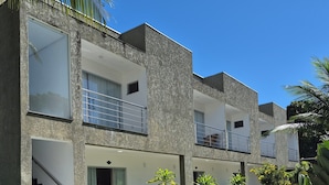 Un edificio moderno de varios pisos con balcones, una zona de estar al aire libre techada y un jardín bien cuidado.