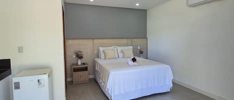 A bedroom with a bed, a nightstand, a refrigerator, and an air conditioning unit.