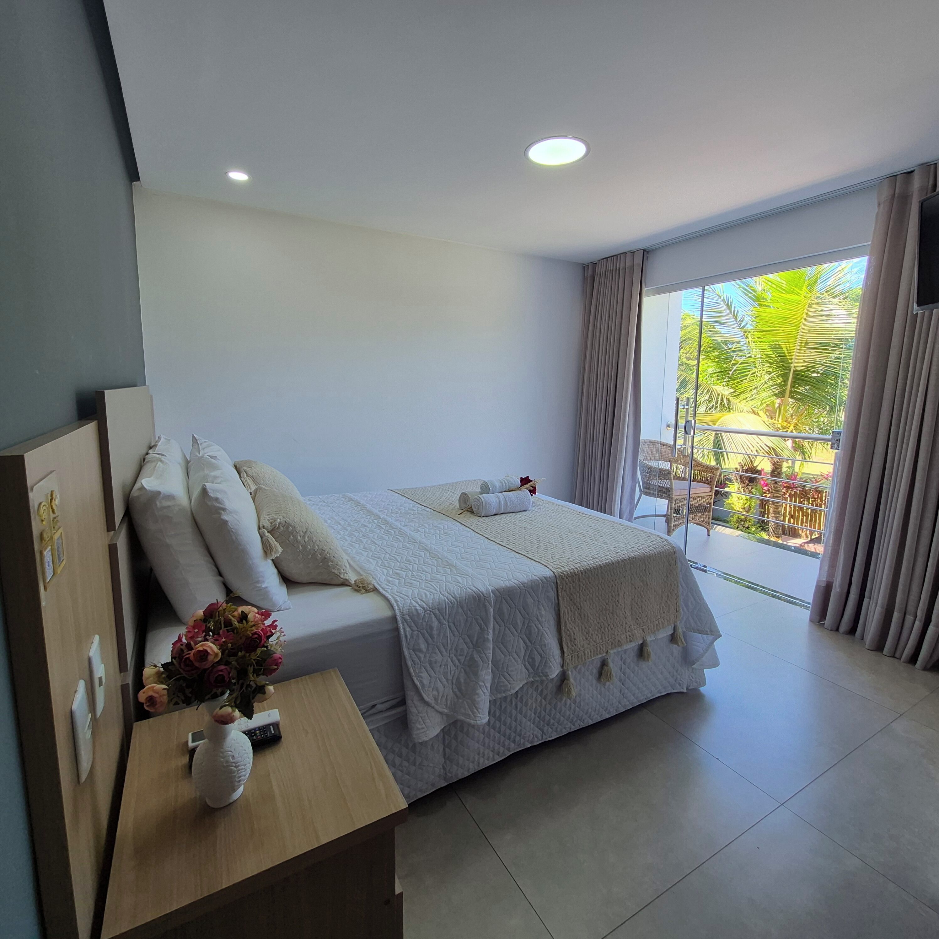 A hotel room with a bed, a desk with a vase of flowers, and a view of the outdoors.