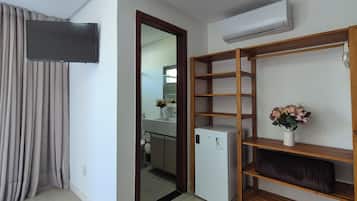 A modern living room with a flat-screen TV, a built-in air conditioner, a wooden shelving unit, and a refrigerator.