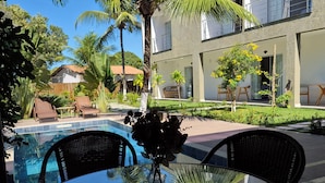 Una mesa de vidrio con sillas de mimbre, una piscina y un patio con vistas a un edificio moderno y palmeras.