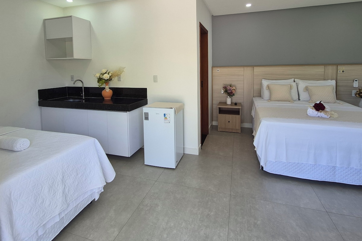 Ein Hotelzimmer mit zwei Betten, einer kleinen Küchenzeile, einem Kühlschrank und einem Badezimmer mit Spiegel.
