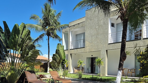 Una piscina con sillones de descanso, palmeras y un edificio de dos pisos con balcones.