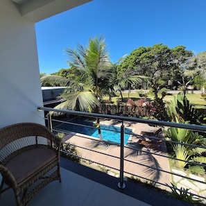 Un balcon avec un fauteuil en osier, une piscine et une végétation luxuriante.