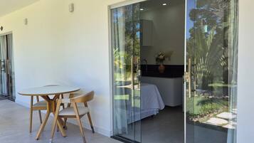 Quarto moderno com porta de vidro deslizante para um jardim, uma pequena mesa redonda com cadeiras e uma cama com cobertura branca.