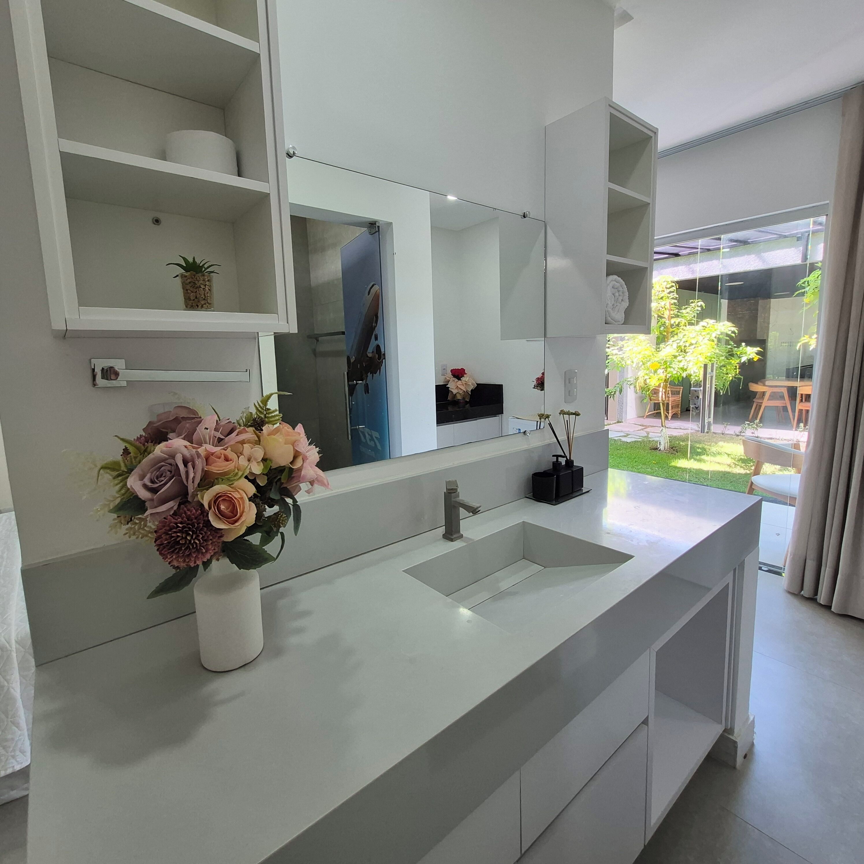 A modern bathroom with a large mirror, a white sink, and a vase of flowers.