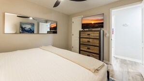 Ein Schlafzimmer mit einem Bett, einer Kommode, einem Spiegel, einem Deckenventilator und einem Fernseher an der Wand.