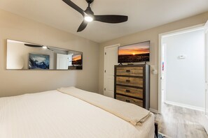 Ein Schlafzimmer mit einem Bett, einer Kommode, einem Spiegel, einem Deckenventilator und einem Fernseher an der Wand.