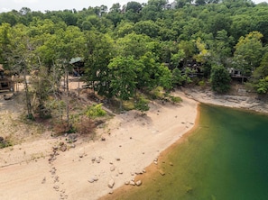 Eine Küstenlandschaft mit Sandstrand, klarem Gewässer und bewaldeten Hügeln im Hintergrund.