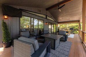 Un espacio de estar techado al aire libre con una mesa, sillas, ventanas amplias y vistas del exterior.